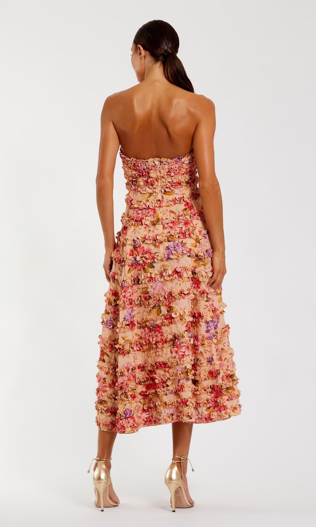 Woman with her back to the camera wears the Mac Duggal 8262 Midi Floral Wedding Guest Dress, a strapless ruffled design paired with metallic heels. A chic choice for any wedding guest.